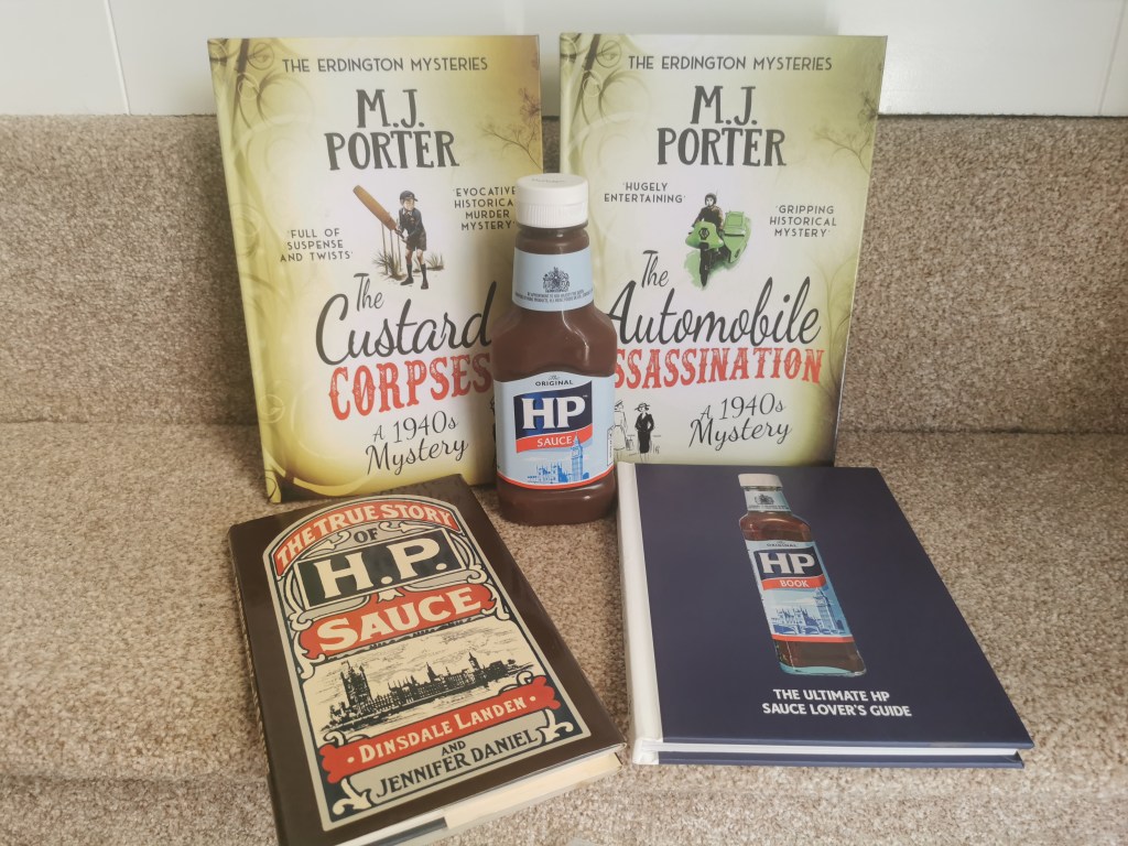 Image sgows a hardback copy of The Custard Corpses and The Automobile Assassination with a bottle of HP Sauce and two books about HP Sauce, The True History of HPSauce and The Ultimate HP Sauce Lover's Guide. 
