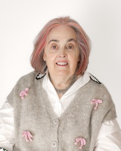 Author Fenella J Miller. A white woman with pink hair wearing a grey and pink cardigan.